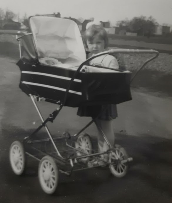 Dziewczynk obok czarnego wózka dziecięcego w stylu retro z białymi pasami i chromowanym stelażem. Wózek z dawnych czasów.